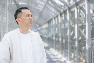 A middle-aged Asian man walks down a glass-walled hallway.