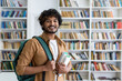 © Liubomir - Portrait of happy satisfied african american student with curly hair, guy with books and backpack standing in university academic library smiling and looking at camera.