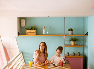 Wall Mural - Mother and daughter having a breakfast with fresh squeezed juices in the cafe