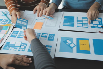 Close up ux developer and ui designer brainstorming about mobile app interface wireframe design on table with customer breif and color code at modern office.Creative digital development agency