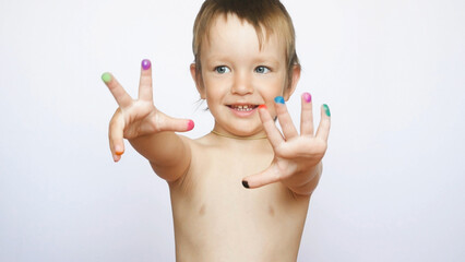 A cute little boy stands with arms extended forward showing his painted multi-colored fingers against white background