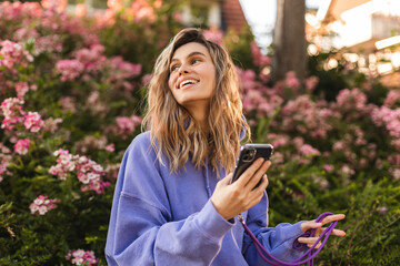 attractive blonde curly woman wear purple hoody hold mobile phone and look at side, look happy and s