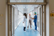 © Maskot - Full length of physician and doctors discussing while standing in corridor at hospital