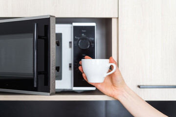 Wall Mural - closeup of woman holding cup near microwave indoors