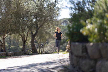 An adult smiling fitness woman jogging in the green park