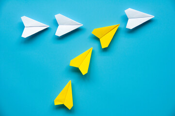 Wall Mural - Yellow paper airplane origami joining other white airplanes on blue background with customizable space for text or ideas. Leadership concept.