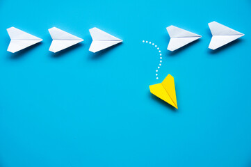 Wall Mural - Yellow paper airplane origami leaving other white airplanes on blue background with customizable space for text or ideas. Leadership concept and copy space.