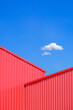 Two red Corrugated metal walls of Warehouse Building interlock in geometric shape against blue sky in vertical frame, Street Minimal architecture Background