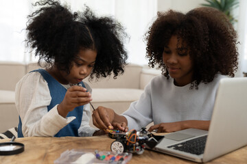 African American female and child girl building automatic toy car technology from online laptop computer. Teacher and child girl learning checking, repairing robotics toy car from online