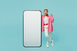 © ViDi Studio - Full body fun young woman wear pink shirt white t-shirt headscarf big huge blank screen mobile cell phone with area point finger up isolated on plain pastel light blue cyan background studio portrait.