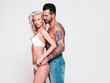 © halayalex - Sexy beautiful woman and her handsome boyfriend. Young passionate couple hugging. Man with nude tattoo torso. Blond model in lace lingerie wearing pure underwear. Posing in studio, near white wall