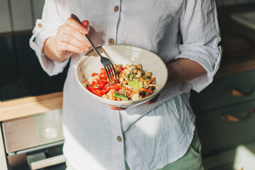 Wall Mural - Young woman eating healthy food sitting in the beautiful interior with green flowers on the background