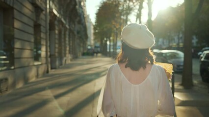 Wall Mural - A young woman in a white beret walks with a bouquet of flowers down a sunny alley in Paris