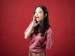 © Daniel - A portrait of a young Indonesian (Asian) woman wearing a pink shirt, appearing to be screaming with her hands over her mouth. Isolated with a red background