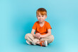 © deagreez - Portrait of positive cheerful boy wear orange stylish clothes relax rest good mood empty space isolated on cyan color background