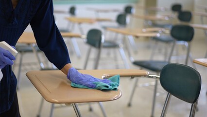 Wall Mural - Teacher back at school after covid-19 quarantine and lockdown, disinfecting desks.