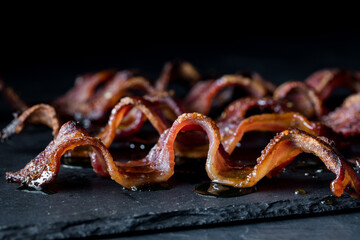 Wall Mural - close up of wavy strips of crispy maple pepper bacon against a dark background.