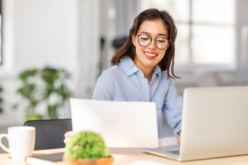 Wall Mural -  young  businesswoman in  glasses holding paper  while sitting at desk with laptop and working on business project in home office.