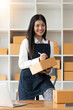 © Natee Meepian - Woman who runs an e-commerce business is writing a list of customers on paper box before shipping to them, Concept of selling products online