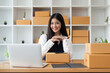 © Natee Meepian - Young pretty asian start up business woman in apron working with online parcel box warehouse selling online product