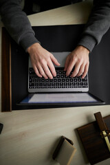 man working on a laptop. top view of human hands are typing on a laptop. Top down view at male hands typing on laptop keyboard while writing code at textured wooden desk in IT development studio