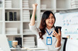© Tj - Portrait of Smiling young female  feel euphoric sitting at she's desk using smart phone at office.