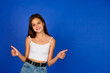 Portrait of smiling teen girl in white t-shirt showing thumbs up at blue background, looking at camera. Positive cute teenage lady expressing good emotion. Human emotional concept. Copy ad text space
