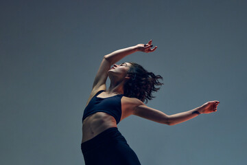 Freedom of movements. Sportive young woman with relief, slim, fit body in sportswear training against grey studio background. Concept of sportive lifestyle, beauty, body care, fitness, health