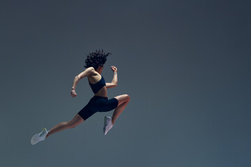 Wall Mural - Athletic art. Dynamic image of sportive woman in motion, jumping, running, training against grey studio background. Concept of sportive lifestyle, beauty, body care, fitness, health