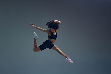 In motion. Art of movement. Attractive young woman with slim, fit body training against grey studio background. Jumping. Concept of sportive lifestyle, beauty, body care, fitness, health