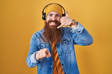 Poster - Caucasian man with long beard listening to music using headphones smiling doing talking on the telephone gesture and pointing to you. call me.