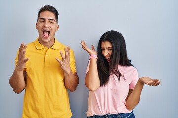 Poster - Young couple standing over isolated background celebrating mad and crazy for success with arms raised and closed eyes screaming excited. winner concept