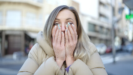 Wall Mural - Young blonde woman standing with surprise expression at street