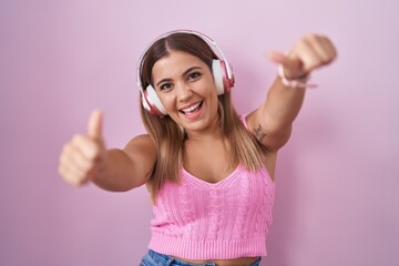 Poster - Young blonde woman listening to music using headphones approving doing positive gesture with hand, thumbs up smiling and happy for success. winner gesture.