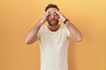 Poster - Middle age man with beard standing over yellow background trying to open eyes with fingers, sleepy and tired for morning fatigue