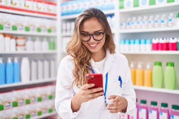 Canvas Print - Young beautiful hispanic woman pharmacist using smartphone working at pharmacy