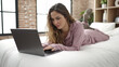 © Krakenimages.com - Young beautiful hispanic woman using laptop lying on bed at bedroom
