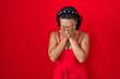 Young hispanic woman standing over red background with sad expression covering face with hands while crying. depression concept.