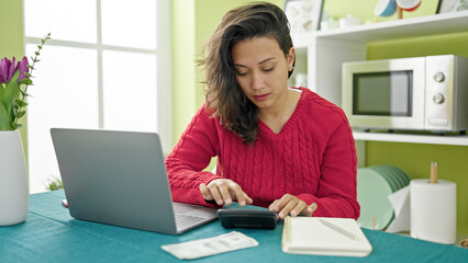 Canvas Print - Young beautiful hispanic woman using laptop counting dollars at dinning room