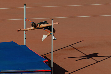 Wall Mural - athlete jumper high jump in summer athletics competition, silhouette high jumper on red track stadium