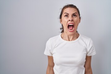 Beautiful brunette woman standing over isolated background angry and mad screaming frustrated and furious, shouting with anger. rage and aggressive concept.