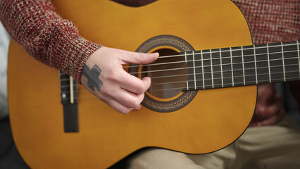 Wall Mural - Young bald man playing classical guitar sitting on sofa at home