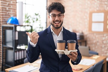 Poster - Hispanic man with beard working at the office holding coffee pointing thumb up to the side smiling happy with open mouth