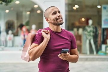 Canvas Print - Young latin man using smartphone holding shopping bag at street