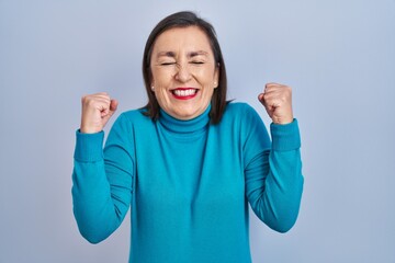 Wall Mural - Middle age hispanic woman standing over isolated background excited for success with arms raised and eyes closed celebrating victory smiling. winner concept.