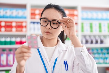 Canvas Print - Young chinese woman pharmacist smiling confident holding pills tablet at pharmacy