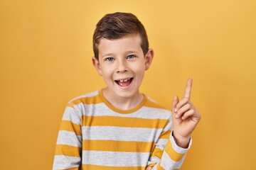 Sticker - Young caucasian kid standing over yellow background with a big smile on face, pointing with hand and finger to the side looking at the camera.