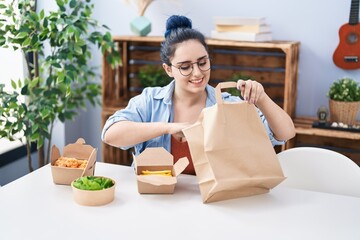 Wall Mural - Young caucasian woman eating take away food sitting on table at home