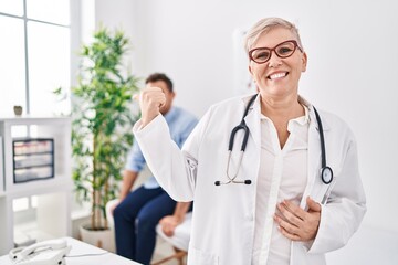 Poster - Female doctor wearing uniform and stethoscope at medical clinic pointing thumb up to the side smiling happy with open mouth