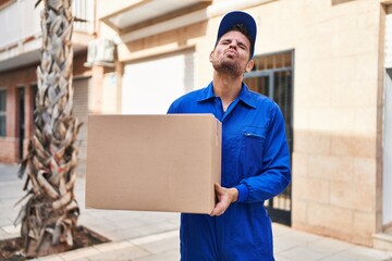 Sticker - Young hispanic man delivering box looking at the camera blowing a kiss being lovely and sexy. love expression.